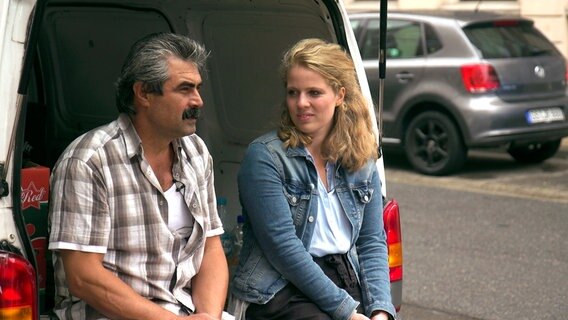 Ein Mann (l.) und eine junge Frau sitzen in einer Kofferraumtür eines Transporters. © NDR/Carina Nickel/Lena Lobers 