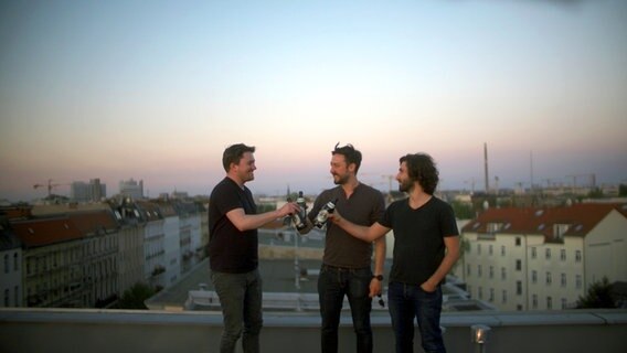 Drei Männer stehen auf einem Dach und trinken Bier. © NDR/Tobias Zwior/Benjamin Arcioli 