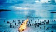 Viele Menschen laufen ins Meer. Am Strand lodert ein großes Lagerfeuer. © NDR 