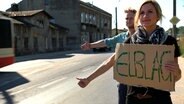 Eine Frau und ein Mann stehen mit einem Pappschild an der Straße und halten die Daumen hoch. © NDR 