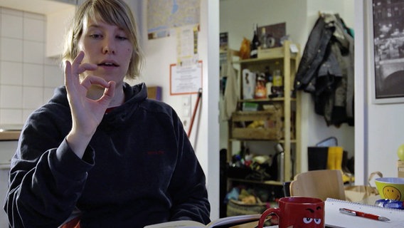 Eine junge Frau sitzt am Tisch und übt Gebärdensprache. Eine junge Frau sitzt am Tisch und übt Gebärdensprache. © NDR/7Tage