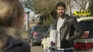 Eine Reporterin im Gespräch mit einem Mann vor seinem Taxi. © NDR/7 Tage 