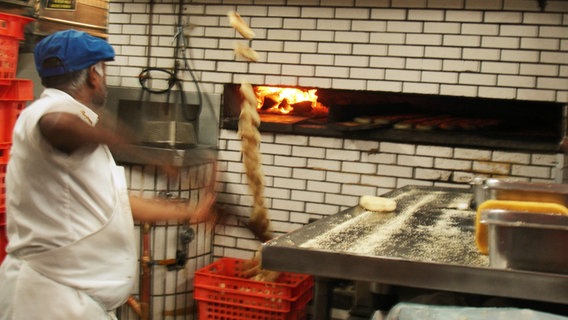 Ein Bäcker wirft gebackene Bagel in eine Kiste © NDR 