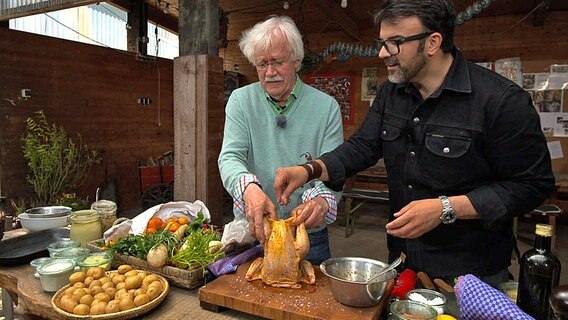 Carlo von Tiedemann (li.) lässt sich von Koch Tarik Rose die Zubereitung von Hühnchen zeigen. © NDR 