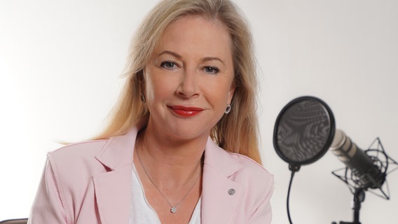 Eine Frau mit blonden, halblangen Haaren und einer hellrosa Jacke sitzt vor einem Mikrofon. Es ist die Finanzexpertin Anne E. Connelly. © Anne Connelly 