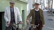 Uli Feick und Sven Dewitz posieren mit ihren historischen Fahrrädern auf einem Bürgersteig. © NDR 