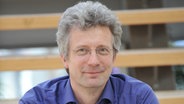 Dr. Tillmann Bendikowski sitzt auf einer Treppe und schaut in die Kamera. © C. Bertelsmann Foto: C. Bertelsmann