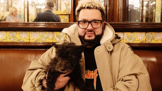 Oliver Polak posiert mit einem Hund auf dem Arm in einem Café. © Gerald von Foris / Suhrkamp Verlag 
