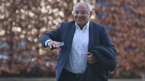 Felix Magath im Gehen, mit einer Jacke und einem Handy in der Hand. © picture alliance / Fußball-News Saarland | Fabian Kleer 