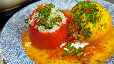 Rote und gelbe Paprika mit Füllungen aus Reis, Grünkohl, Kohlwurst oder Lachs mit Tomantensud und Petersilie auf einem Teller serviert. © NDR Foto: Florian Kruck