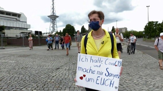Karoline Preisler von der FDP steht mit Mundschutz und einem Schild auf einem Platz © NDR Foto: Screenshot