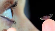 Eine Frau setzt sich eine Kontaktlinse ein. © picture-alliance/chromorange 