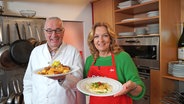 Rainer Sass und Bettina Tietjen stehen in einer Küche und halten Teller mit Nudelgerichten in die Kamera. © NDR/dmfilm/Florian Kruck 