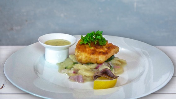 Baked fish is served on a plate with potato salad and remoulade.  © NDR/dmfilm 