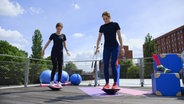Physiotherapeutin Svea Köhlmoos und ihre junge Patientin stehen auf Balancekreiseln. © NDR 
