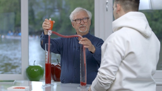 Ernährungs-Doc Jörn Klasen hantiert mit zwei Röhren, die mit roter Flüssigkeit gefüllt, um seinem Patienten Bluthochdruck zu veranschaulichen. © NDR Foto: Moritz Schwarz/Oliver Zydek