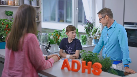 Ernährungsmediziner Matthias Riedl steht mit einem etwa 12-jährigen Jungen und dessen Mutter in der Küche am Tresen. © NDR Foto: Oliver Zydek/Moritz Schwarz