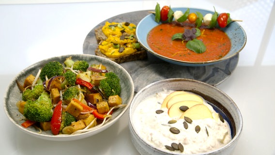 Zu sehen sind ein Teller Tomatenkaltschale, ein Schälchen Joghurt mit Obst und Weizenkeimen, ein Teller Brokkoli-Tofu-Wok und zwei Scheiben Leinsamenbrot mit Kürbisaufstrich. Zu sehen sind ein Teller Tomatenkaltschale, ein Schälchen Joghurt mit Obst und Weizenkeimen, ein Teller Brokkoli-Tofu-Wok und zwei Scheiben Leinsamenbrot mit Kürbisaufstrich. © NDR Foto: Moritz Schwarz/Oliver Zydek