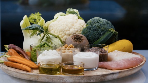 Verschiedene gesunde Lebensmittel wie Gemüse, Joghurt und Öle stehen oder liegen auf einer Holzplatte. © NDR 