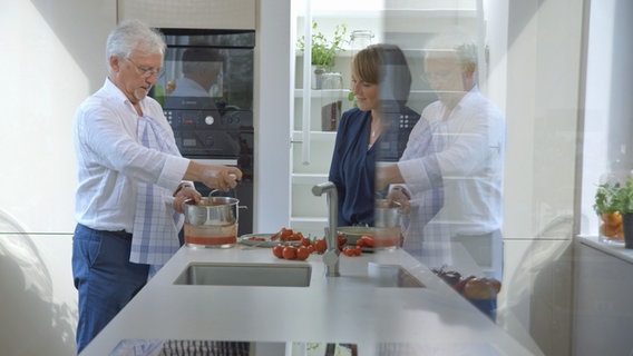 Dr. Jörn Klasen kocht in der Hausboot-Küche etwas mit Tomaten; Patientin schaut zu. © NDR 
