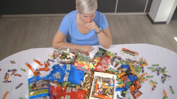 Frau sitzt nachdenklich vor einem Tisch voller Süßigkeiten. © NDR 
