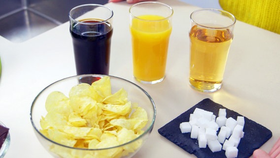 Juice, soft drinks and sweets are on a table, along with a bowl of chips.  © NDR 