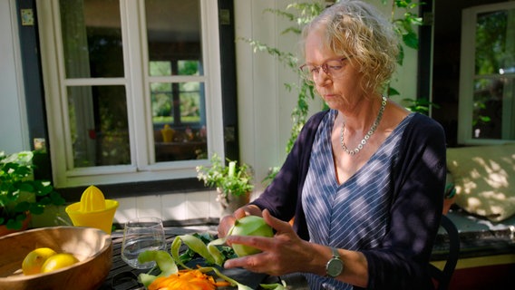 Eine Frau schält Gemüse am Gartentisch. © NDR/nonfictionplanet/Moritz Schwarz 