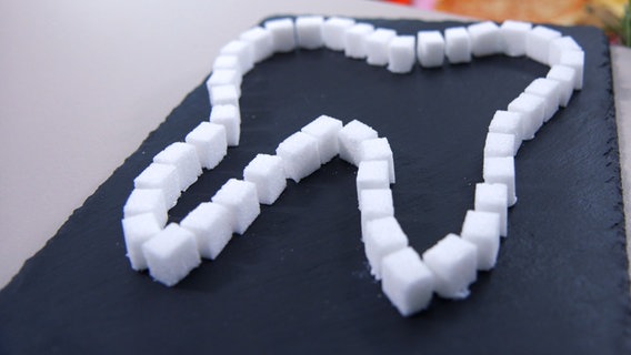 Aus Zuckerwürfeln ist ein Zahnsymbol auf den Tisch gelegt. © NDR Foto: Moritz Schwarz/Oliver Zydek