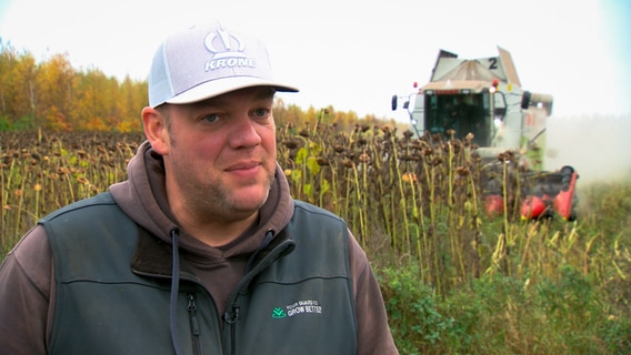 Thomas Andresen auf dem Feld, im Hintergrund eine Landmaschine. © NDR 