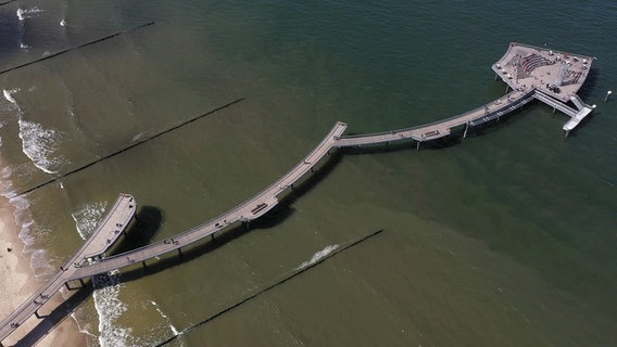 Kein gerader Holzsteg ins Meer und kein imposantes Brückenhaus, sondern ein Kunstwerk aus Stahl: die Seebrücke von Koserow. Die ungewöhnliche Wellenstruktur lässt sich am besten aus der Luft bewundern. Mittlerweile ein sehr beliebter Ort zum Flanieren und Verweilen, mit Sekt und Aperol Spritz. © NDR 