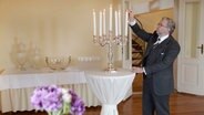 Schlossherr Armin Hoeck zündet die Kerzen eines Silberleuchters an. © NDR 