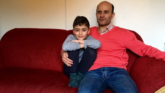 Ahmad hält seinen Sohn Mani im Arm, während die beiden auf dem Sofa sitzen.  