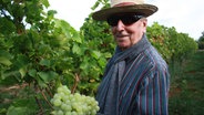 Ein Mann hält große Weintrauben hoch. © NDR/PIXELGALAXIE 