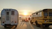 Der Schulbus-Camper und ein klassischer, silberner US-Camper stehen an einem Strand. Die Sonne geht unter. © NDR/Kimmo Wiemann 