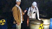 Der "Hausmeister" Johannes Schlüter und ein Arbeiter untersuchen Atommüllfässer.  