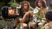 Szene aus Dennis und Jesko: Fernseh-Kontrollmonitor zeigt Neandertaler in einer Höhle © NDR Foto: Christian Merten