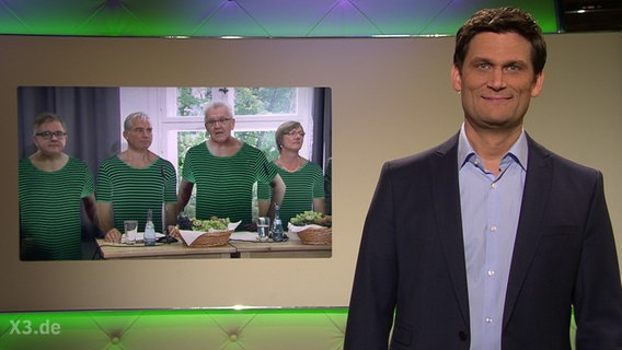 Christian Ehring steht vor einer Montage der grün-schwarzen Koalitionäre, die grün-schwarze Ringelhemden tragen.  Foto: Screenshot