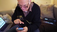 Ein älterer Herr an seinem Smartphone, im Hintergrund Laptop und Tablet.  