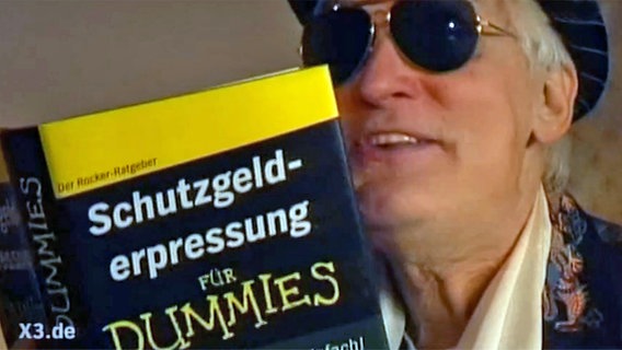 Ein Mann hält das Buch "Schutzgelderpressung für Dummies" in den Händen.  
