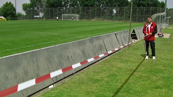 Ein Mann steht mit Absperrband neben einem Fußballplatz. © NDR Foto: Screenshot