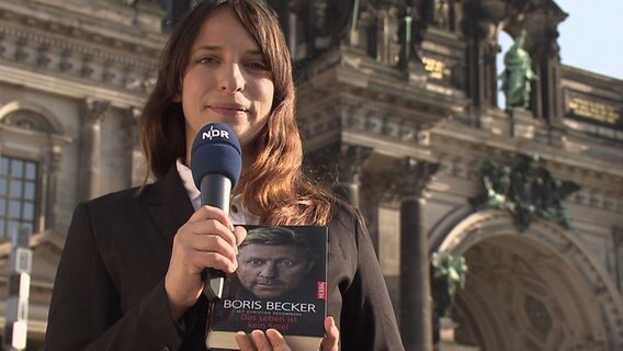Caro Korneli hält vor dem Berliner Dom Boris Beckers Buch "Das Leben ist kein Spiel" in die Kamera. © NDR Foto: Screenshot