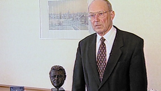Bürgermeister Pöpel steht neben einer Büste von Franz-Josef Strauß. © NDR Foto: Screenshot