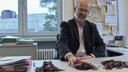 Arno Traut vom Abfallwirtschaftsbetrieb Oldenburg sortiert auf seinem Schreibtisch Laubhaufen. © NDR Foto: Screenshot