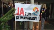 Tobi Schlegl rollt ein Plakat mit der Aufschrift "Ja zum Klimawandel" aus. © NDR Foto: Screenshot
