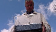 Ein Mann hält eine durchsichtige Kiste mit Regenwürmern. © NDR Foto: Screenshot