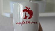 Ein Tasse mit einem Apfelsymbol und der Aufschrift "Apfelkind".  