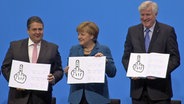 Sigmar Gabriel, Angela Merkel und Horst Seehofer halten auf der Fotomontage jeweils einen Zettel hoch, auf denen Stinkefinger abgebildet sind. © NDR Foto: Screenshot