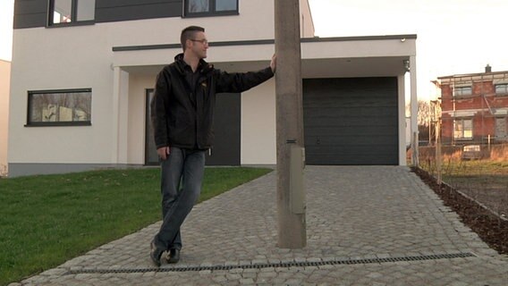 Ein Mann lehnt an einer Laterne, die inmitten seiner Garagenauffahrt steht. © NDR Foto: Screenshot