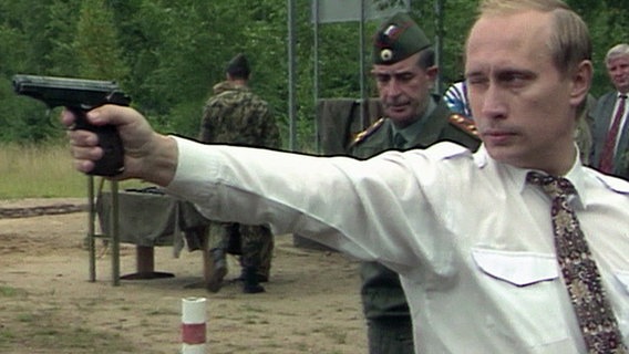 Wladimir Putin zielt mit einer Pistole und kneift dabei sein rechtes Auge zu.  Foto: Screenshot