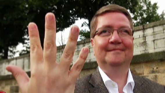 Der sächsische NPD-Spitzenkandidat Symanski hält fünf Finger in die Kamera. © NDR Foto: Screenshot